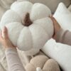 Ręcznie robiona poduszka dynia z miękkiego materiału boucle, z wypełnieniem, trzymana w dłoniach - produkt Simonila z jesiennej kolekcji