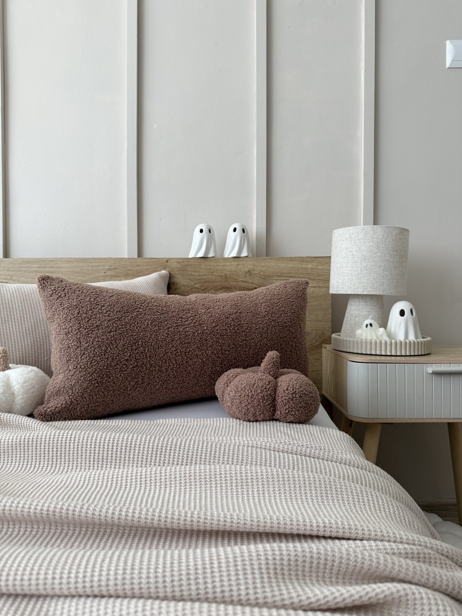 Poduszka z miękkiej dzianiny boucle w ciepłym brązie, leżąca na łóżku z przodu, prezentująca kształt i elegancki design