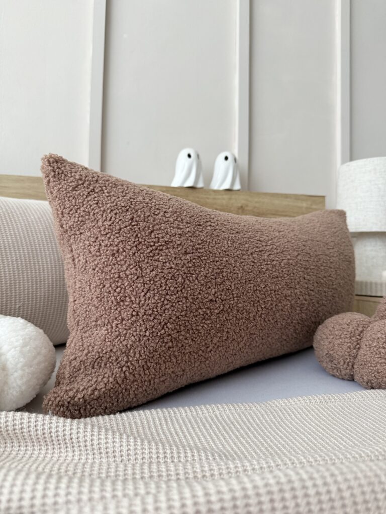 Detal poduszki z dzianiny boucle w brązie, pokazujący miękką puszystą strukturę i przyjemny w dotyku materiał premium