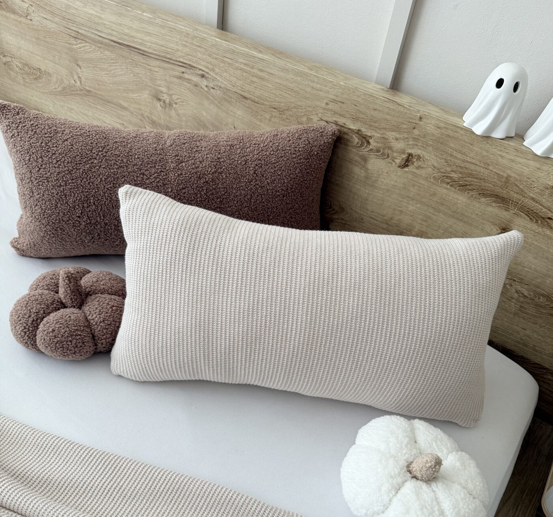 Poduszka z miękkiej dzianiny boucle w ciepłym brązie, ułożona u góry łóżka, prezentująca elegancki i przytulny wygląd sypialni