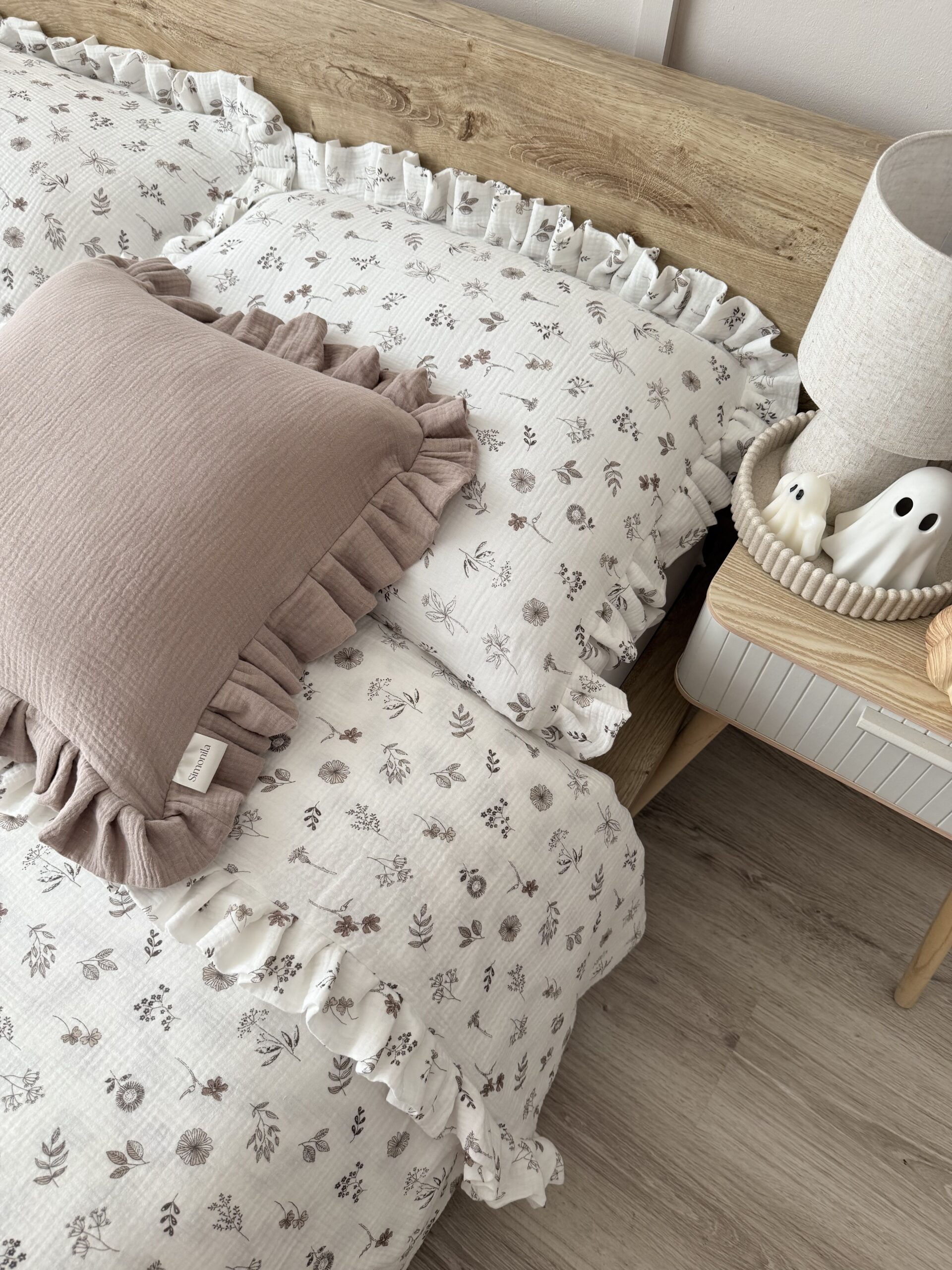 Biały komplet pościeli muślinowej z beżowymi kwiatuszkami i falbanką, elegancko ułożony na łóżku w sypialni