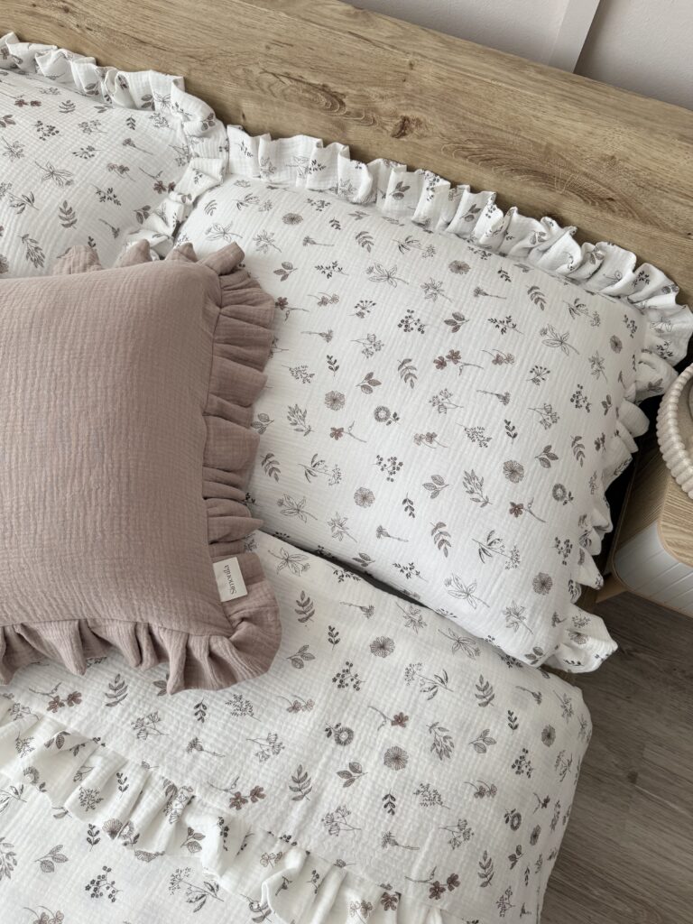 Biały komplet pościeli muślinowej z beżowymi kwiatuszkami i falbanką, elegancko ułożony na łóżku w sypialni