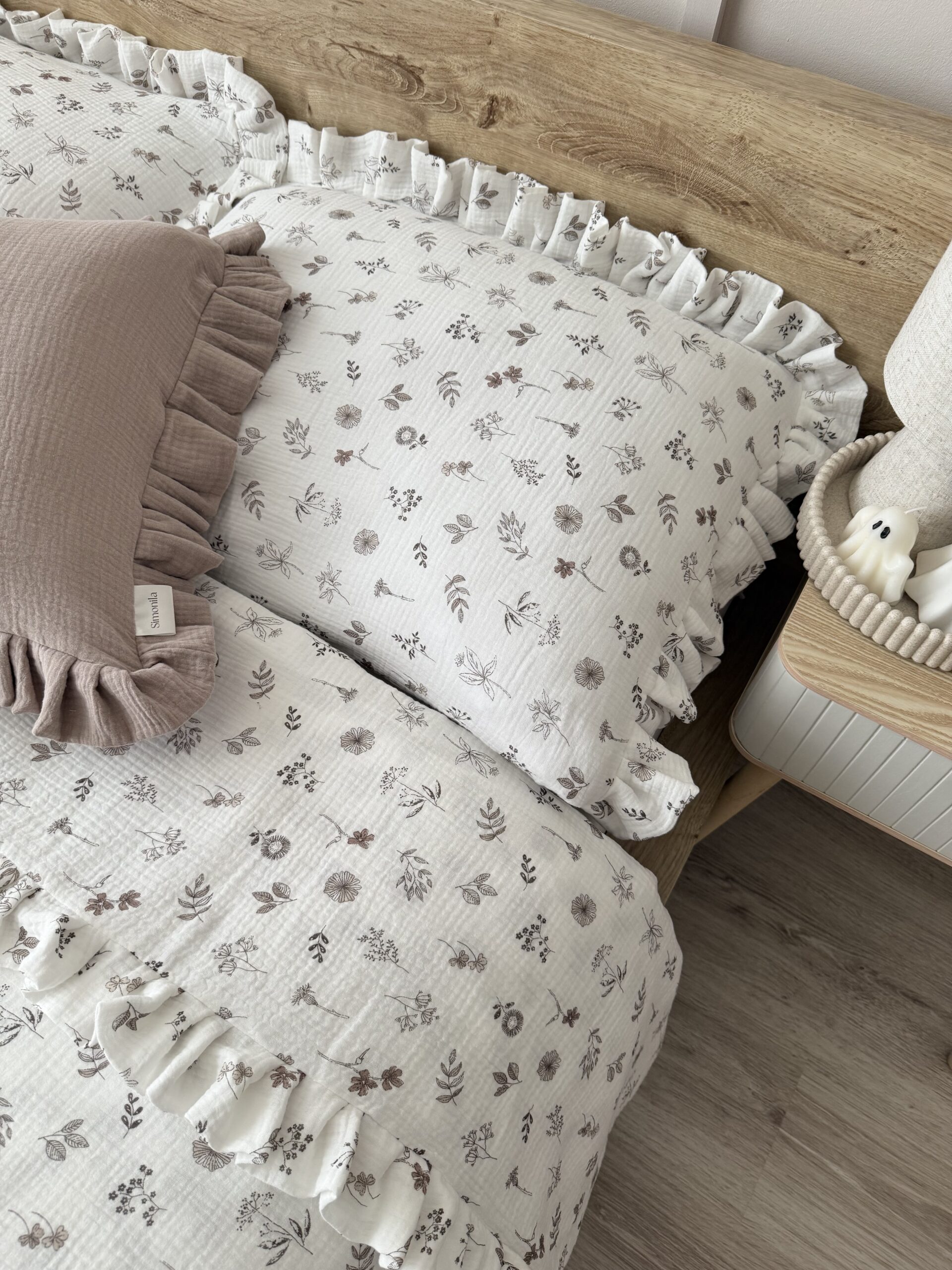 Biały komplet pościeli muślinowej z falbanką i delikatnym wzorem beżowych kwiatuszków, ułożony na łóżku w sypialni