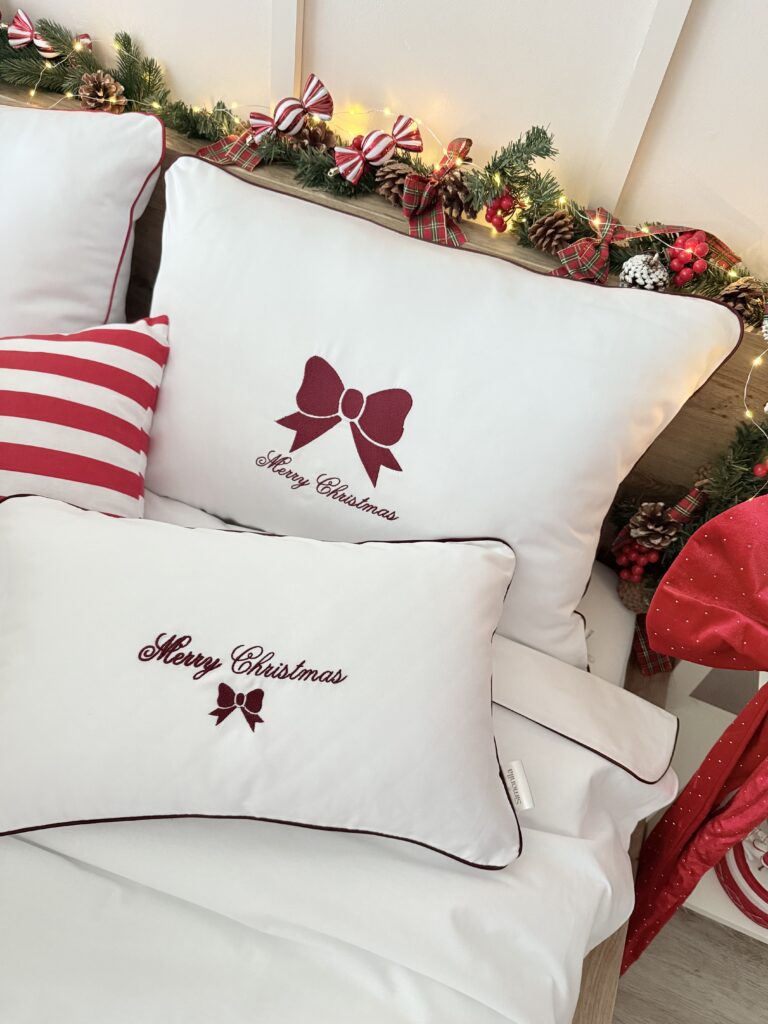 Detal haftu na pościeli – bordowa kokarda Merry Christmas na białej bawełnie, wykonana precyzyjnym haftem maszynowym