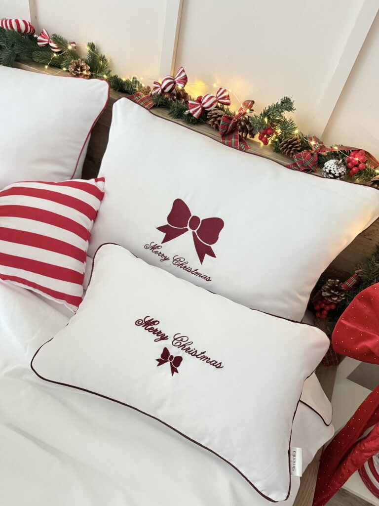Detal haftu na pościeli – bordowa kokarda Merry Christmas na białej bawełnie, wykonana precyzyjnym haftem maszynowym